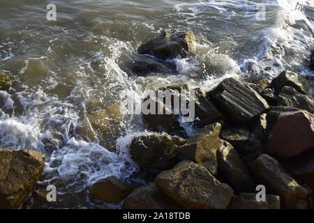 Sea surf, the blue wave hits the rocks. Coastline foam from breaking on the rocks of the sea surf. Wet stones and waves. Background of sea stones and Stock Photo