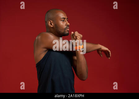 Before workout. Strong young afro american man in sports clothing stretching while standing against red background. Sport concept. Active and healthy lifestyle Stock Photo