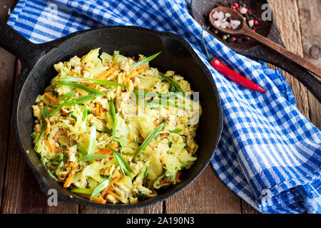Stewed cabbage with pork, carrot, onion and turmeric in black skillet on rustic wooden table Stock Photo