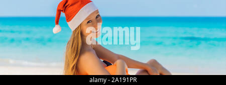 Woman on an inflatable beach couch and Christmas hat on the beach under an umbrella BANNER, LONG FORMAT Stock Photo