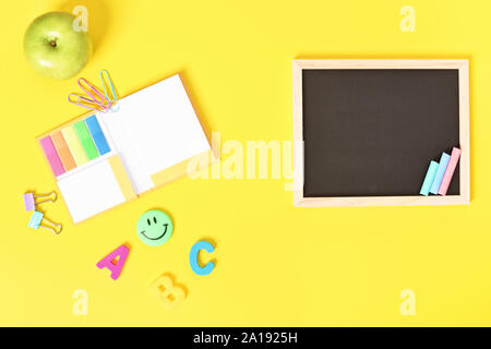 Chalkboard with wooden frame and colorful chalks and school stationeries, isolated on yellow background. Stock Photo