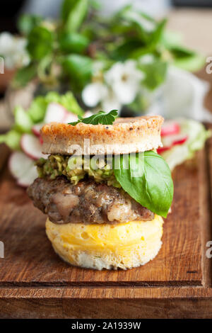 Homemade gluten free burger with eggs bun, beef patty, guacamole and fresh basil leaf on rustic wooden cutting board Stock Photo
