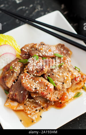 Stir-fried pork with kimchi served with sesame seeds and chopped onion on black table Stock Photo