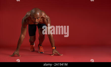 Never stop Portrait of young african man in sportswear going to run while sitting isolated over red background. Fitness and work out concept. Horizontal shot Stock Photo