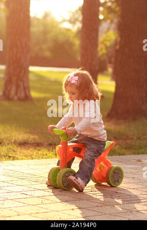 Little girl riding a small bike in the sunlit summer park Stock Photo