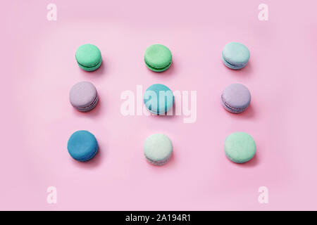 Top view of multicolored sweet macaroon biscuits lying in three lines on pastel pink background. Stock Photo