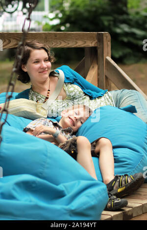 Mother and son swinging on a huge wooden swing with blue bean bags outdoors in the park Stock Photo