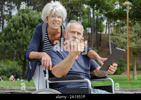 elderly couple outdoors with tablet pc man in wheelchair Stock Photo