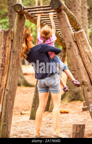 Mother Supporting daughter in the playground with climbing and hanging on a ladder. Stock Photo