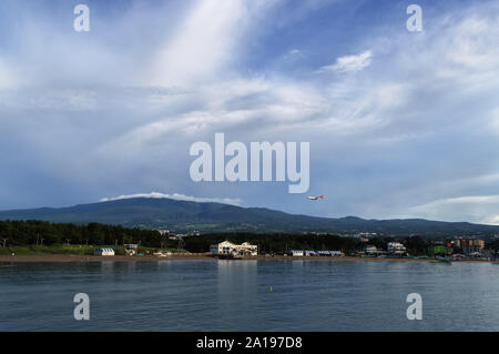 airplane flying over Iho Tewoo Beach on Jeju island with Hallasan mountain and scenic cloudscape on background Stock Photo