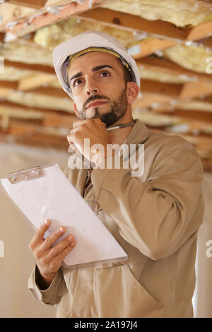 young handsome builder thinking about something while holding clipboard Stock Photo