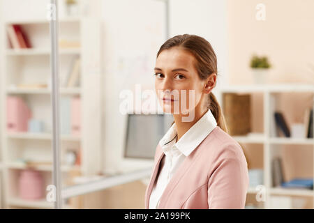 Portrait of young office worker in pink formal suit looking at camera with serious expression at office Stock Photo