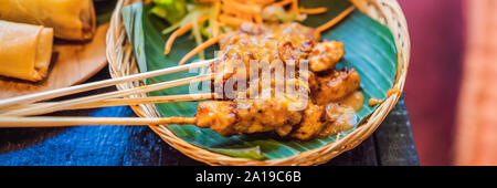 Satay or sate, skewered and grilled meat, served with peanut sauce, cucumber and ketupat. Traditional Malaysian and Indonesian food. Asian cuisine Stock Photo