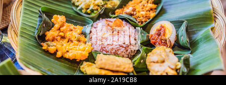 Nasi lemak, Nasi campur, Indonesian Balinese rice with potato fritter, sate lilit, fried tofu, spicy boiled eggs, and peanut BANNER, LONG FORMAT Stock Photo