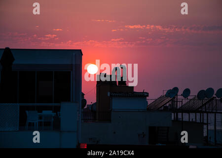 The sun setting behind the rooftops of buildings making the sky purple. Stock Photo