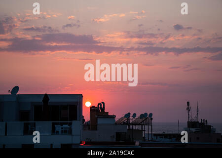 The sun setting behind the rooftops of buildings making the sky purple. Stock Photo