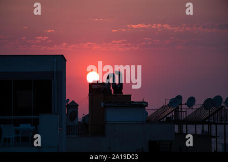 The sun setting behind the rooftops of buildings making the sky purple. Stock Photo