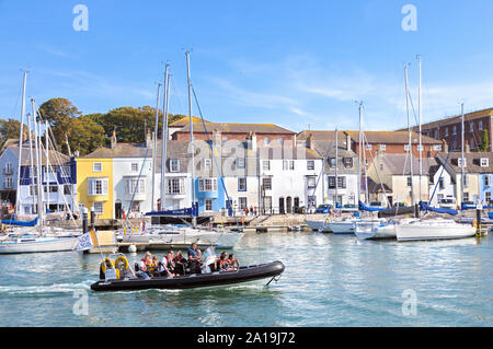 Tourists on a RIB boat trip in the Old Harbour passing the yachts and terraced cottages on Nothe Parade, Weymouth, Jurassic Coast, Dorset, England, UK Stock Photo