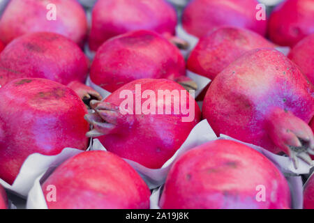 Lots of ripe red pomegranates in a box on a supermarket counter for sale. Stock Photo