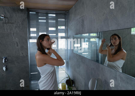 Young brunette woman brushing her hair in a modern bathroom Stock Photo
