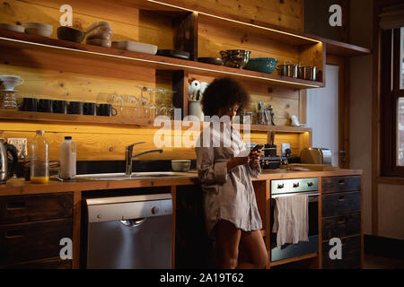 Young woman using smartphone in kitchen Stock Photo