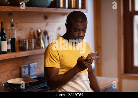 Young man using smartphone in kitchen Stock Photo