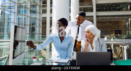 Male and females executives discussing over computer at desk Stock Photo