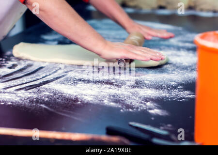 A chef rolls out the doughon on black table. Stock Photo