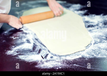 A chef rolls out the doughon on black table. Stock Photo