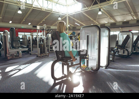 Disabled active senior woman exercising with leg curl machine in fitness studio Stock Photo