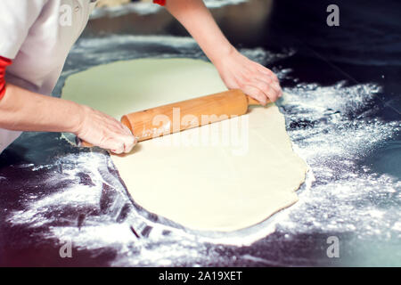A chef rolls out the doughon on black table. Stock Photo