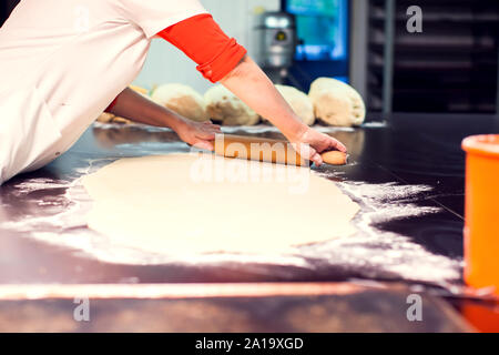 A chef rolls out the doughon on black table. Stock Photo