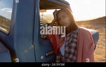 Portrait of a young woman leaning on a pick-up truck during a stop off on a road trip Stock Photo