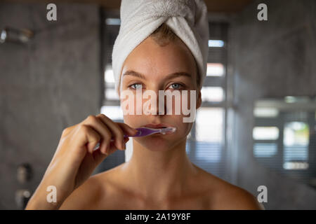 Young blonde woman brushing her teeth with her hair wrapped in a towel Stock Photo
