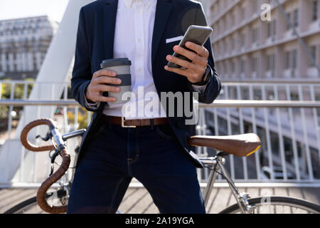 Young professional man using smartphone and leaning on his bike Stock Photo