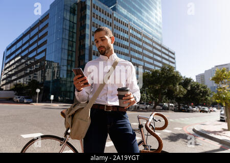 Young professional man using smartphone and leaning on his bike Stock Photo