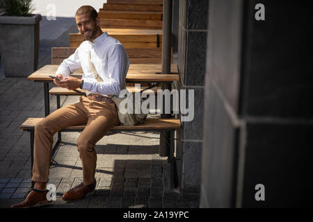 Young professional man using smartphone sitting outside Stock Photo
