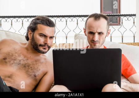 Two men working remotely from home on laptop in a balcony on a sunny day. Freelancing concept. Stock Photo