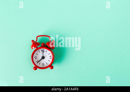 Red small alarm clock on mint color background with copy space. Minimal style flat lay. Time management concept. Horizontal. Stock Photo