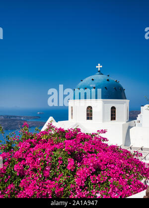 Majestic view of Nikolaus monastery with domed church and pink flowers on seashore of Santorini island in Greece Stock Photo