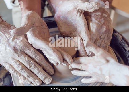 Potter's hands guiding child's and woman's hands to help him to work with the pottery wheel. Stock Photo