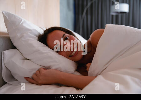 Young brunette woman lying in bed and smiling Stock Photo
