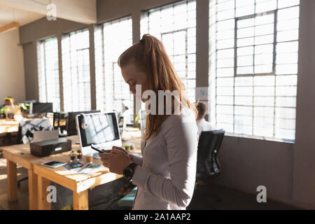Young creative professional woman using smartphone  in a sunlit office Stock Photo