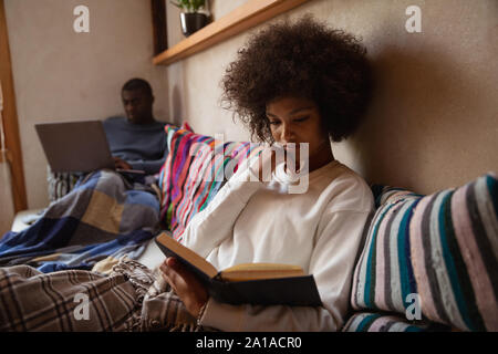 Woman reading on a sofa and man using laptop Stock Photo