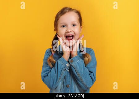 Cheerful emotional little girl on a yellow background. The child is pleased with the good news. Stock Photo