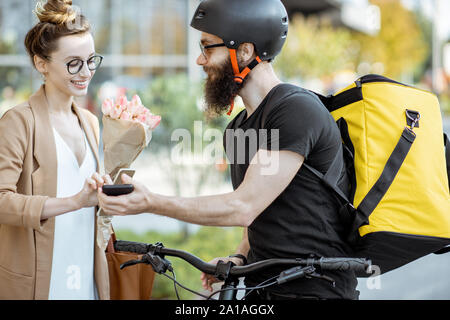 Courier delivering fresh flowers to a young business woman on a bicycle wearing delivery backpack. Fresh floral delivery concept Stock Photo