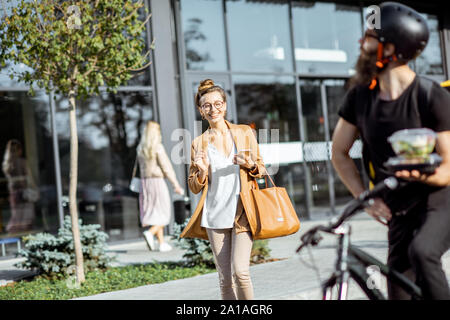 Business woman walking out the office to a courier delivering takeaway food Stock Photo