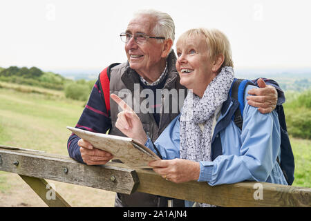 Retired Senior Couple On Walking Holiday Resting On Gate Looking At Map Stock Photo