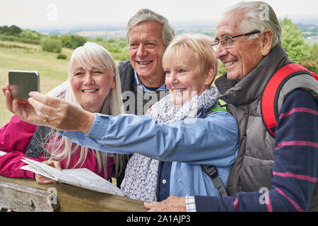 Group Of Senior Friends Hiking In Countryside Standing By Gate  And Taking Selfie On Mobile Phone Stock Photo