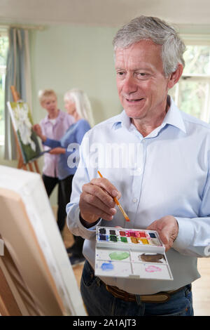 Senior Man Attending Painting Class With Teacher In Background Stock Photo